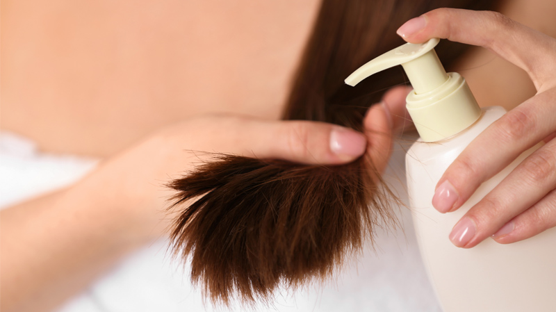 Katgegorie Bild für Pflegeprodukte Eine Frau hält mit einer Hand eine große Strähne ihrer rotbraunen Haare und in der anderen eine Flasche mit Haarpflegemittel, die sie gleich auftragen wird