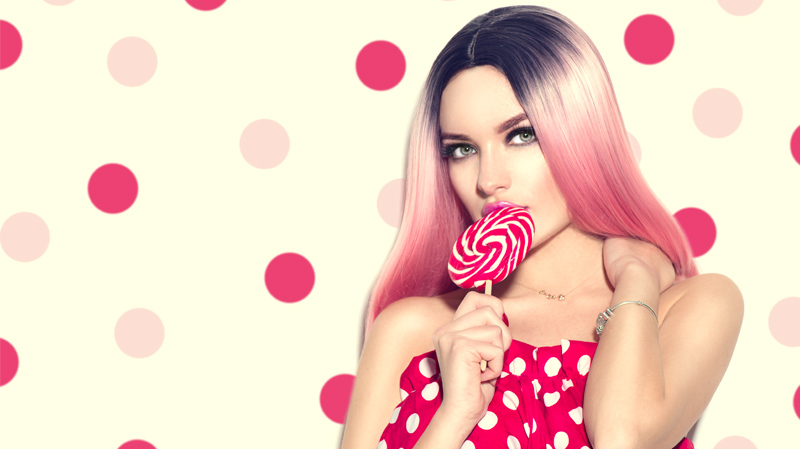 Kategorie Bild für Sales Produkte Eine Frau mit glatten Haaren im Ombre Stil von Schwarz bis Rosa verlauf hat einen roten Riesen-Lolli in der Hand. Sie trägt ein roten Kleid mit weißen Punkten und steht vor einer beigen Wand mit roten und rosa Punkten